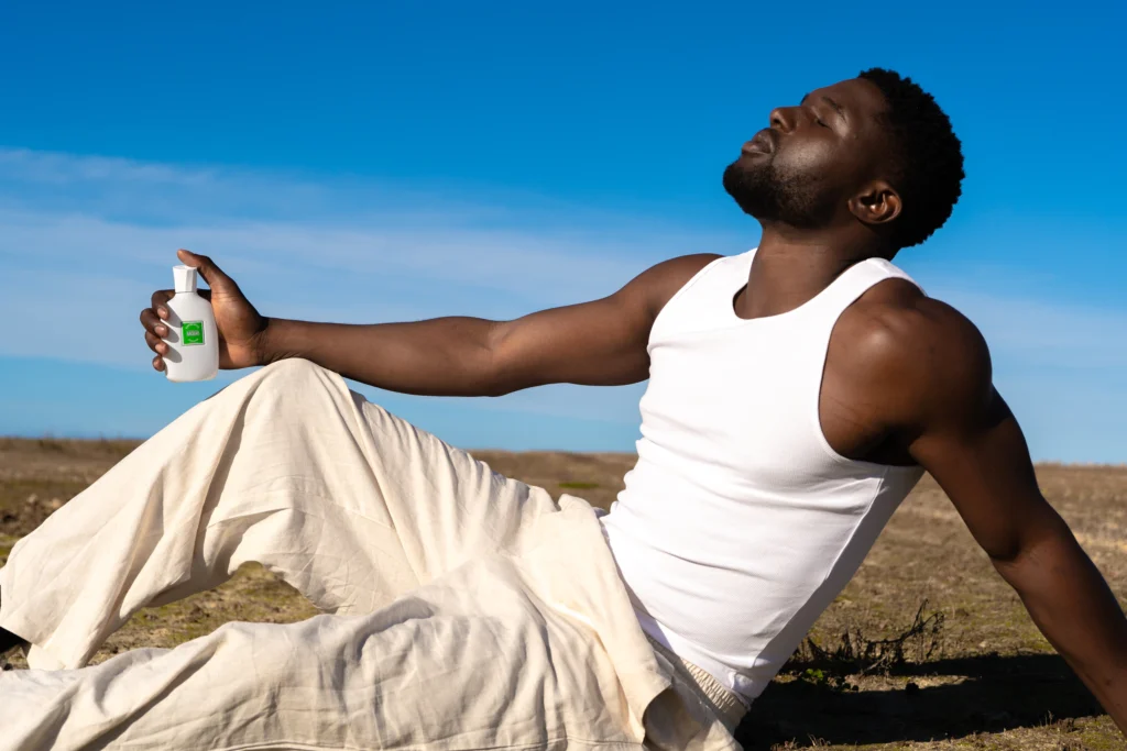 Homme vaporisant Les murmures du Baobab, allongé sous un ciel bleu