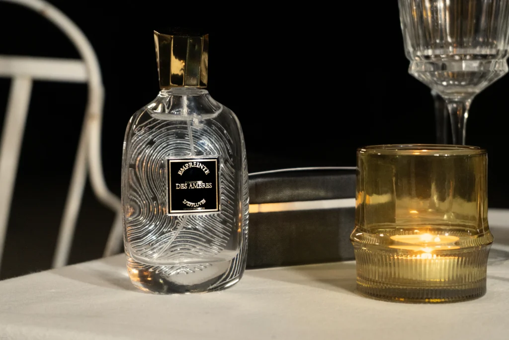 Flacon Symphonie des ambres près de verres en cristal, à la lueur d'une bougie